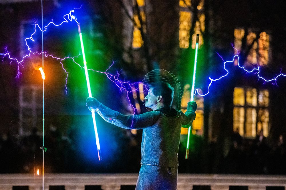 Man holding glowing tubes as electricity sparks around him